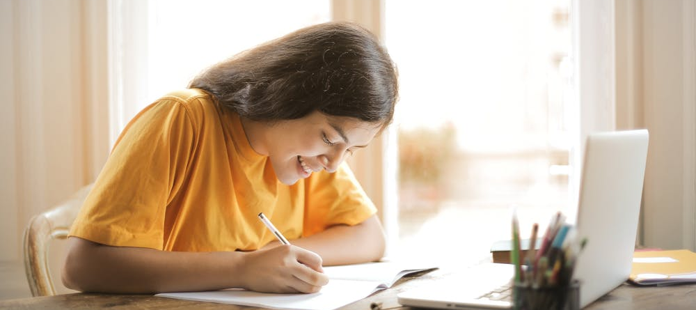 Student in yellow shirt writing on white paper